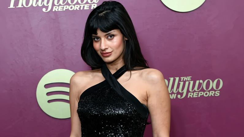 Jameela Jamil in a black sequined dress, posing at an event with "The Hollywood Reporter" and Spotify logos.