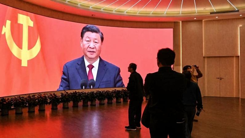People are silhouetted in front of a large screen displaying an image of Xi Jinping.