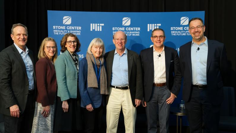 Seven people stand smiling in front of a blue MIT Stone Center backdrop