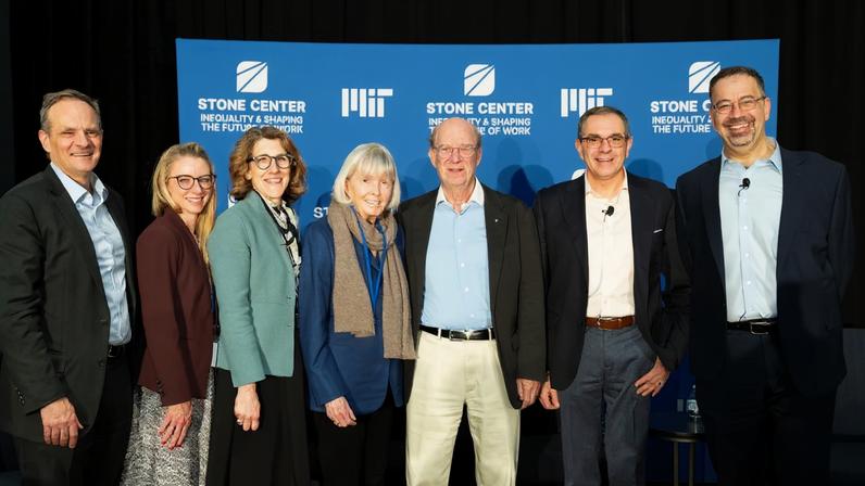 Seven people stand smiling in front of a blue MIT Stone Center backdrop