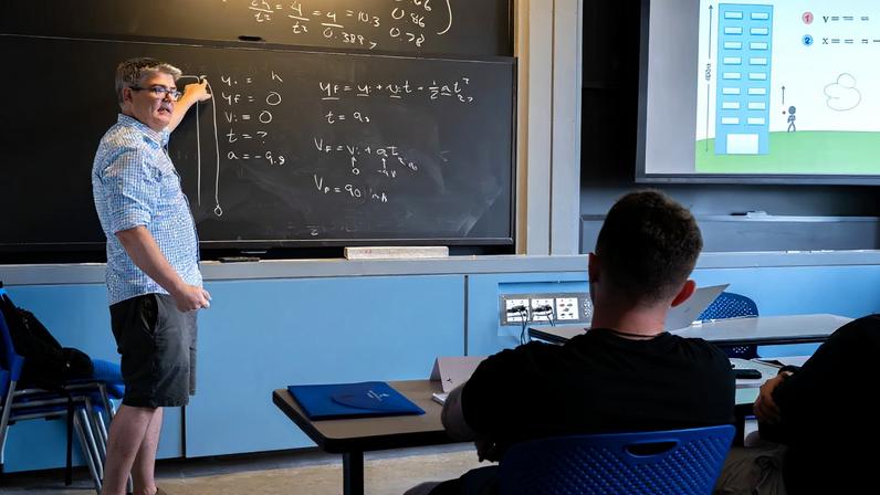 Michael McDonald stands at a chalkboard, lecturing in a classroom
