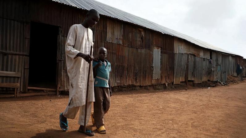 A disabled man walking with a cane and help from his child.
