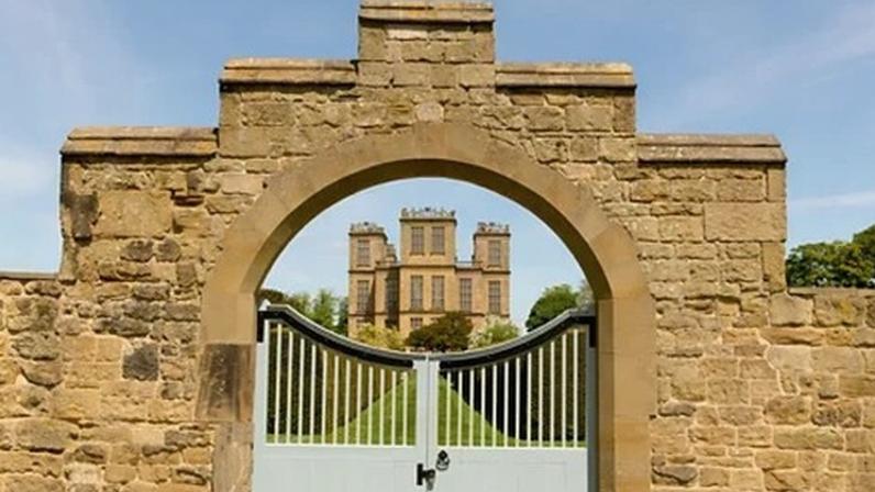 Alamy A stately home is seen through closed gates in a stone wall (Credit: Alamy)