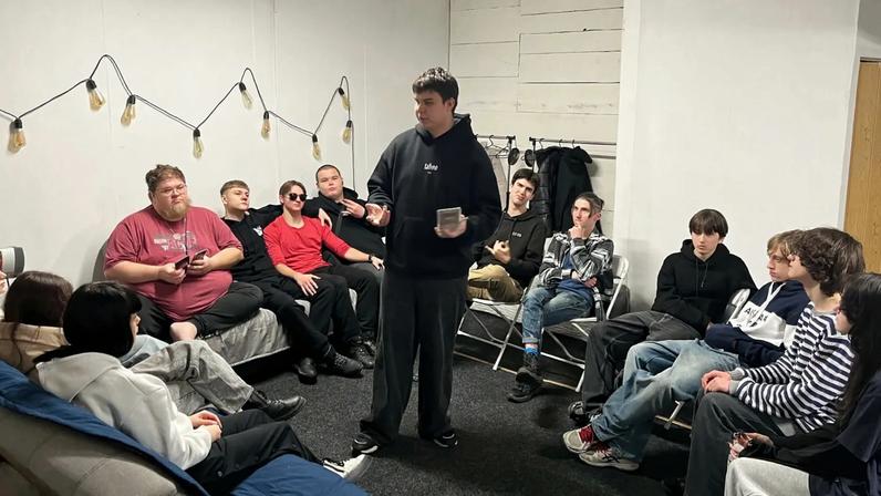 Pastor Alex Zaytsev, on the end of the couch in a red shirt, hosting his teen ministry.