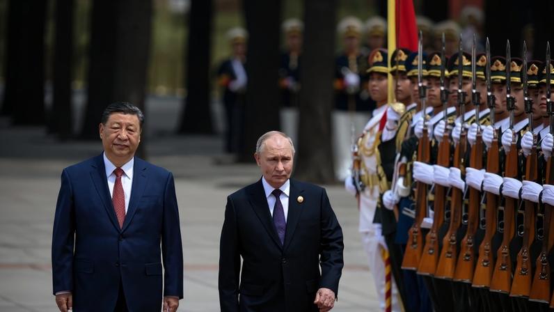 Russian President Vladimir Putin and Chinese President Xi Jinping, both wearing dark suits, walk in front of a line of Chinese soldiers dressed in uniform, sporting rifles.
