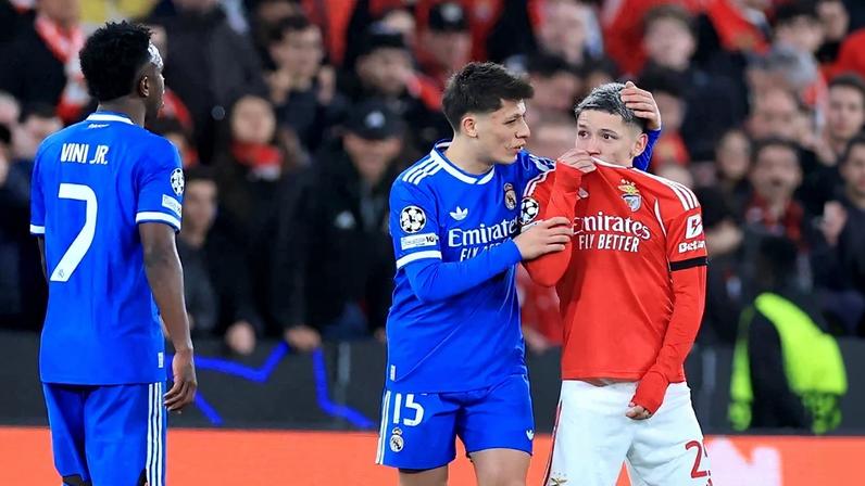 O atacante argentino do Benfica, número 25, Gianluca Prestianni, cobre a boca enquanto discute com o atacante brasileiro do Real Madrid, número 7, Vinicius Junior, que se queixou de supostos insultos racistas durante o jogo de ida da fase eliminatória da Liga dos Campeões. Foto: PATRICIA DE MELO MOREIRA / AFP