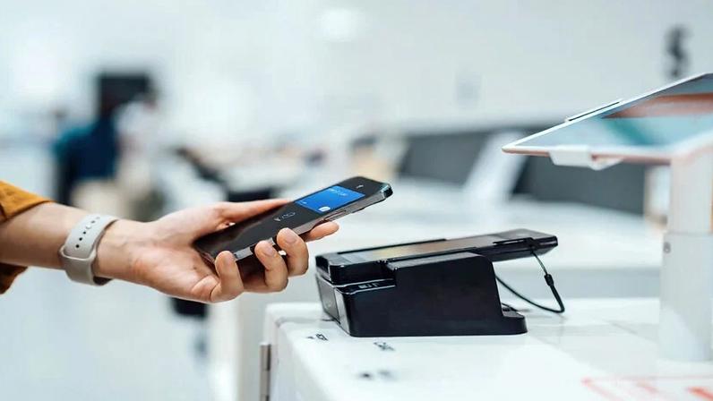 Uma mão segura um smartphone próximo a uma máquina de cartão de crédito.