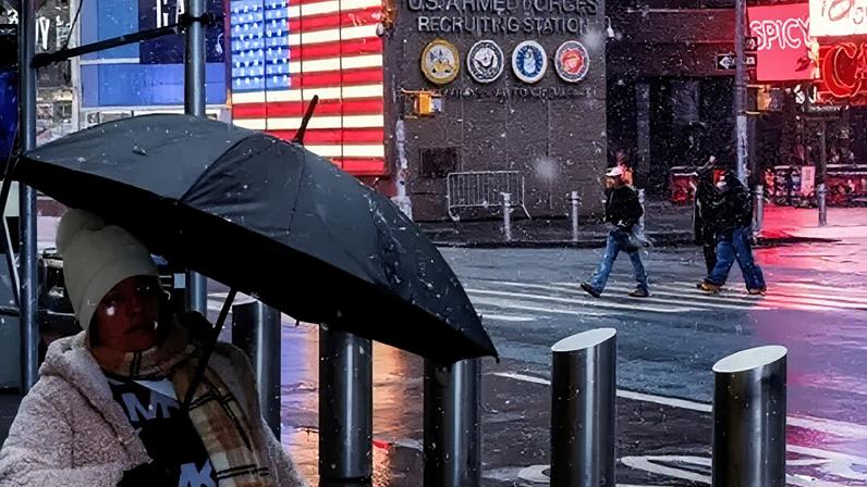 People walk through Times Square as snow falls during a winter storm in New York City on 22 February 2026.