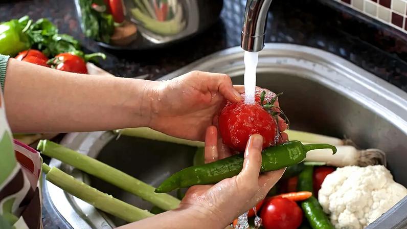 Fotografia de uma mulher lavando legumes na cozinha.