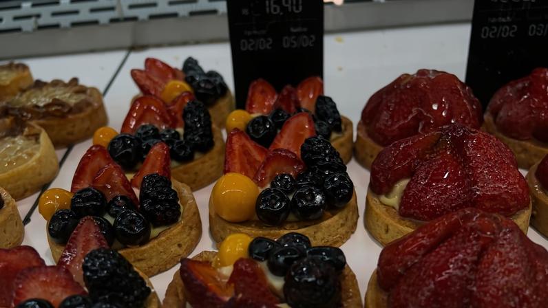 Várias tortinhas individuais expostas em vitrine, algumas com morangos, mirtilos, amoras e physalis, outras cobertas com morangos inteiros brilhantes.