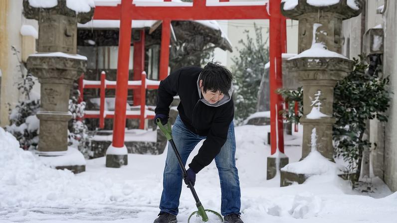 Homem limpa a neve na frente de templo em Tottori, Japão 25/01/2023. Mandatory credit Kyodo/via REUTERS