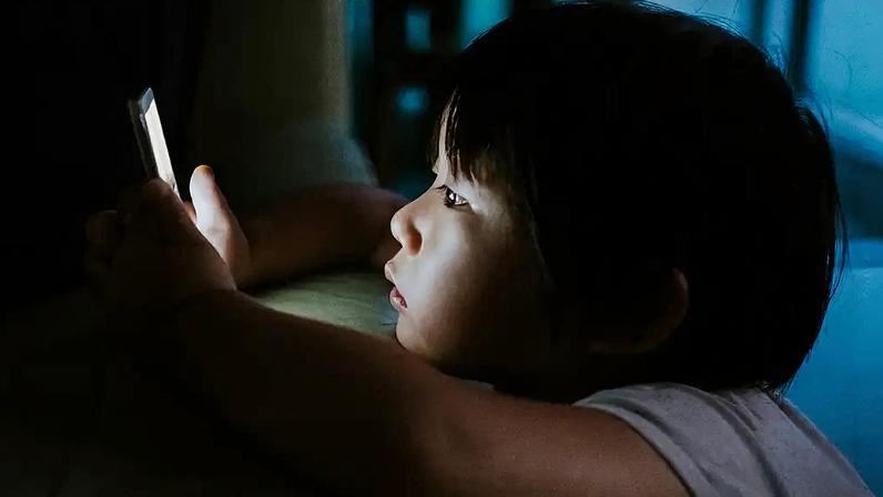 Fotografia de uma criança vidrada no celular.