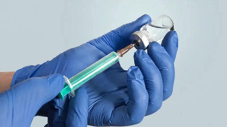 Fotografia de médico segurando um frasco com uma médicamento e uma agulha.