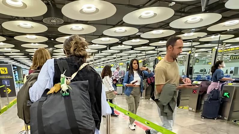 People queue in marked-out lines to go through automatic passport control gates under a ceiling with circular lamps