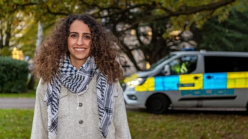Huda Ammori outside smiling with police van in the background