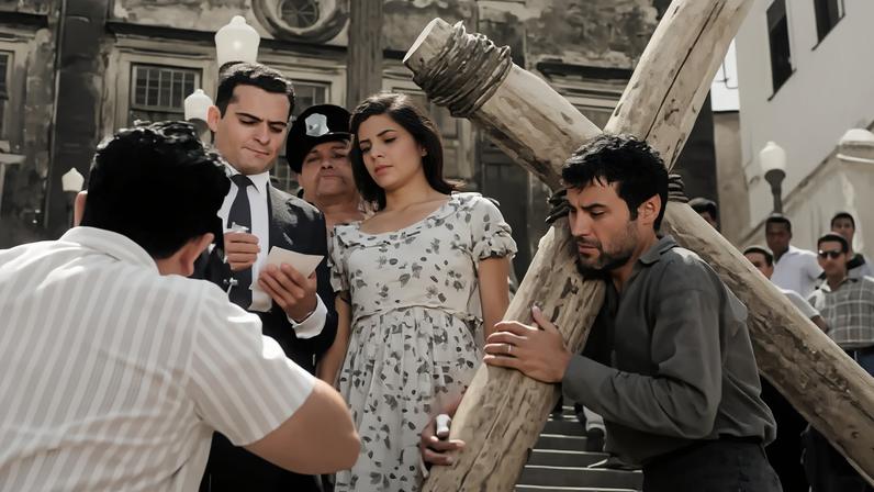 Imagem da cena do filme "O Pagador de Promessas" em que o personagem principal está carregando uma cruz.