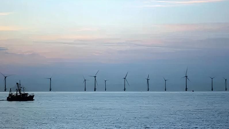 PA Media Wind turbines in the sea on the horizon. A trawler is moving from left to right in the foreground.