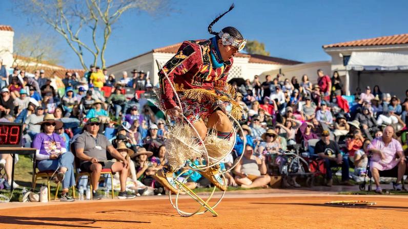 A competitor clad in colourful traditional regalia wows the crowd with their dance moves incorporating wooden hoops during the 2025 World Championship Hoop Dance Contest at the Heard Museum