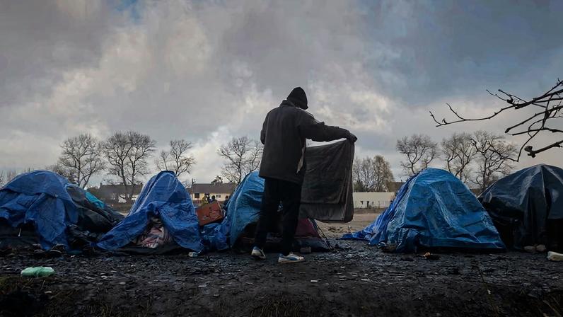A refugee folds his blanket at a migrant camp