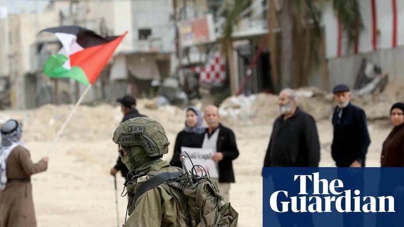 An Israeli soldier walks past displaced Palestinians protesting to demand the right to return to their homes, in the Nur Shams refugee camp in Tulkarm, West Bank.