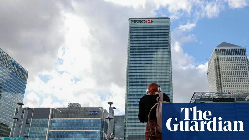View of tall office blocks in Canary Wharf, London, including the HSBC and Barclays buildings. The photograph is taken from the platform of Poplar station. A red-haired woman stands with her back to the camera , leaning as if she is looking at her phone. She has large headphones on and carries a rucksack over one shoulder