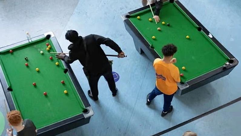 Overhead view of young people playing on two pool tables in a youth centre
