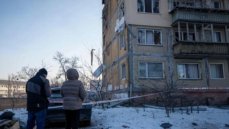 People look at a damaged apartment building in the snow