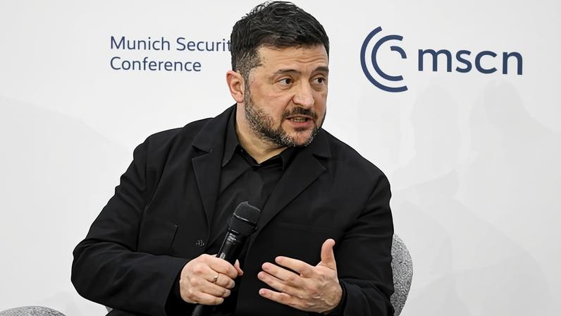 Ukraine’s president, Volodymyr Zelenskyy, sitting with a microphone in front of a sign saying Munich Security Conference