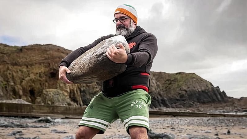 David Keohan lifting a huge stone on a beach in County Waterford.