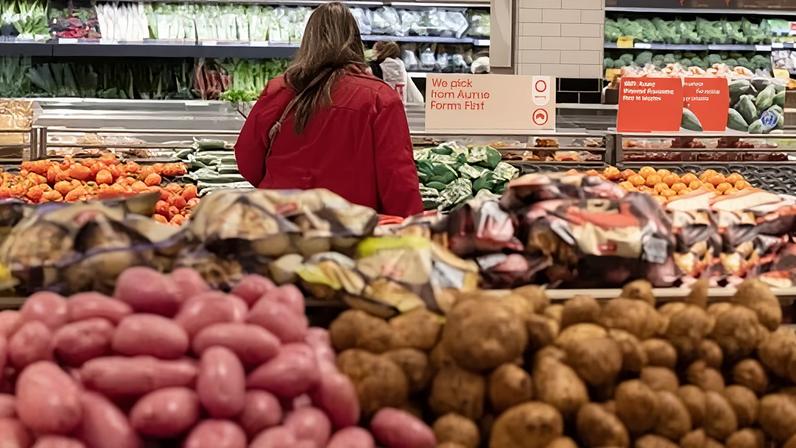 A person shopping in the fresh fruit and vegetable section of a supermarket with piles of potatoes in the foreground