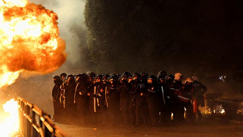 Law enforcement officers stand guard behind crowd-control barriers as a Molotov cocktail explodes outside the Prime Minister's office during an anti-government protest triggered by a corruption investigation into Deputy Prime Minister Belinda Balluku, in Tirana, Albania.