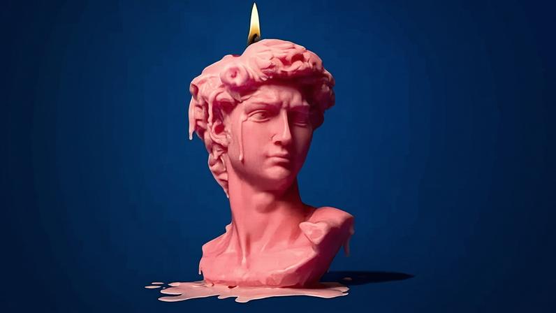 A lit pink candle in the shape of the head of Michelangelo's David, with wax dripping down, on a dark blue background.