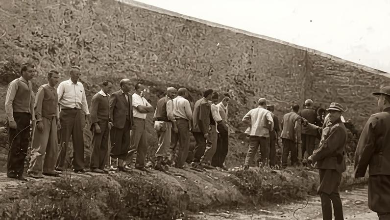 Black and white photo of men lined up along a wall