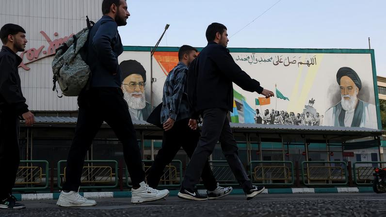 People walk near a mural featuring images of Iran's leaders in Tehran