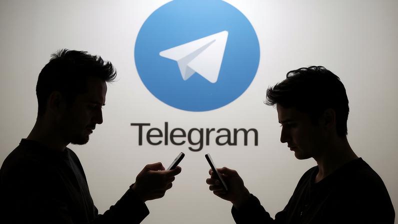 Two men pose with smartphones in front of a screen showing the Telegram logo in this picture illustration taken in Zenica