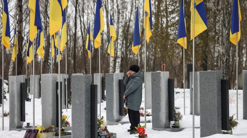 A woman reacts as she stands in front of a grave at a local cemetery, as she pays tribute to the victims of the Russian attack on Ukraine