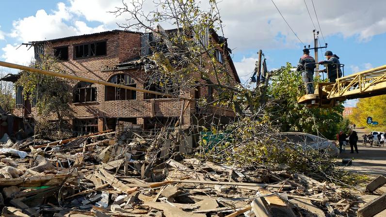 Workers fix wires in front of a damaged house following what Russian-installed authorities described as an overnight Ukrainian missile strike, amid the Russia-Ukraine military conflict in Yasynuvata (Yasinovataya) in the Donetsk region, a Russian-controlled area of Ukraine, October 26, 2025. REUTERS/Alexander Ermochenko