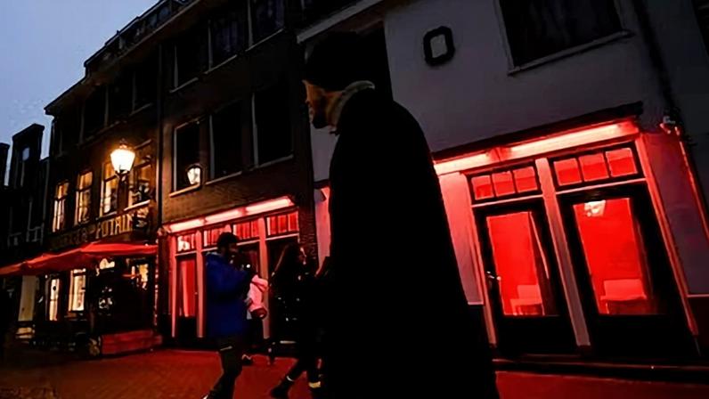 Varias personas caminan cerca de un local con luces rojas, en el Barrio Rojo de Ámsterdam (Países Bajos), en diciembre de 2022.