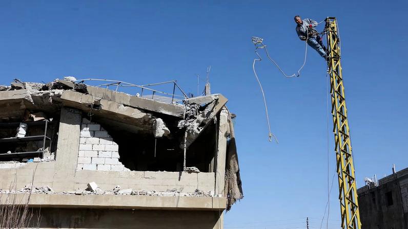 A man works on an electric pole next to a damaged building, in the aftermath of an Israeli strike on friday, in Tamnine el Tahta, Bekaa valley, Lebanon, February 21, 2026. REUTERS/Mohamed Azakir