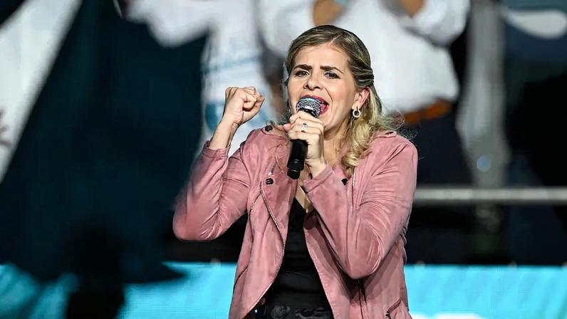 Costa Rican presidential candidate Laura Fernandez gestures as she speaks into a microphone. She is wearing a pink jacket.