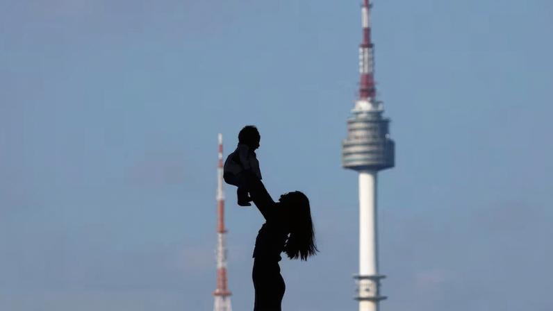 A woman holding up her baby is silhouetted against the backdrop of N Seoul Tower in Seoul