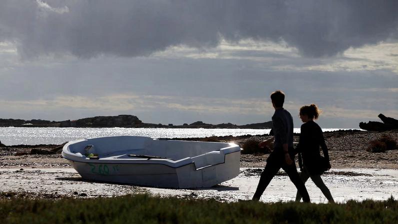 People walk next to a discarded boat used by migrants to reach Mallorca rests on Es Caragol beach in the south of the Balearic island, in Santanyi, Mallorca, Spain, November 20, 2025.