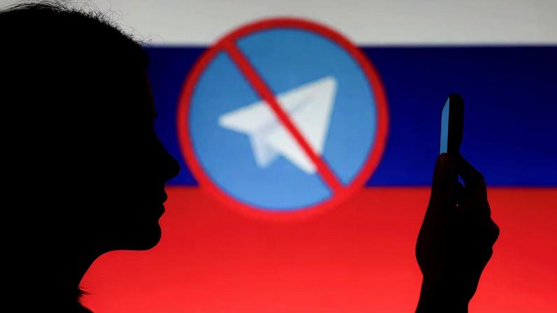 A woman poses for a photo while holding a smartphone next to a screen showing the crossed logo of Telegram messaging app against the backdrop of the Russian state flag, in this illustration taken February 12, 2026.