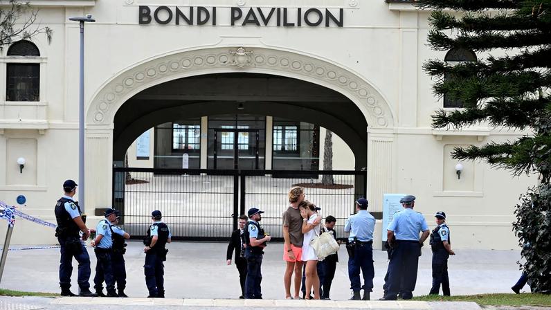 Two people embrace as police officers stand guard outside Bondi Pavilion following the attack on a Jewish holiday celebration at Sydney's Bondi Beach, in Sydney, Australia, December 15, 2025.