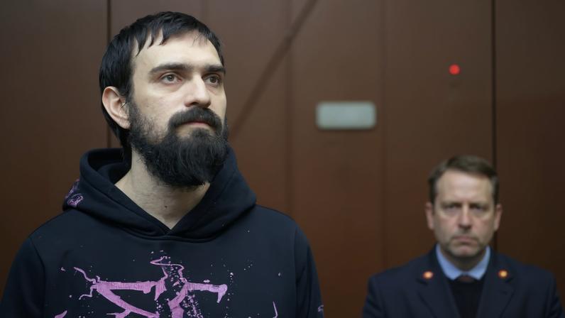 Russian comedian Artemy Ostanin stands behind a glass wall in an enclosure for defendants during a court hearing after his March 2025 arrest over a stand‑up performance, in Moscow, Russia, February 4, 2026.