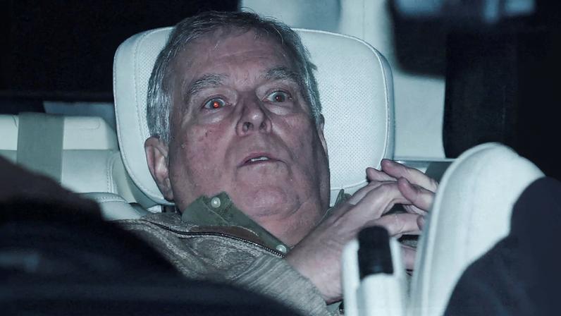 Prince Andrew in a car, looking forward with red eyes due to camera flash.