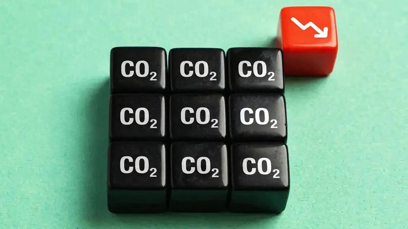 Imagem, em fundo verde, de nove cubos pretos perfilados com a inscrição CO2. No alto, vê-se outro cubo vermelho com uma seta branca apontada para baixo.