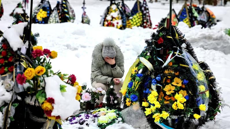 A woman reacts as she sits in front of a grave at a local cemetery, decorated with flowers to pay tribute to the victims of the Russian attack on Ukraine, in Chernihiv