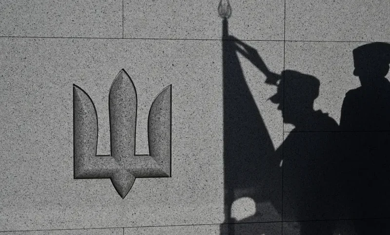 Shadows of honor guard service members are cast on a wall beside the Ukrainian trident during a funeral ceremony for unidentified soldiers at the National Military Memorial Cemetery near Kyiv.