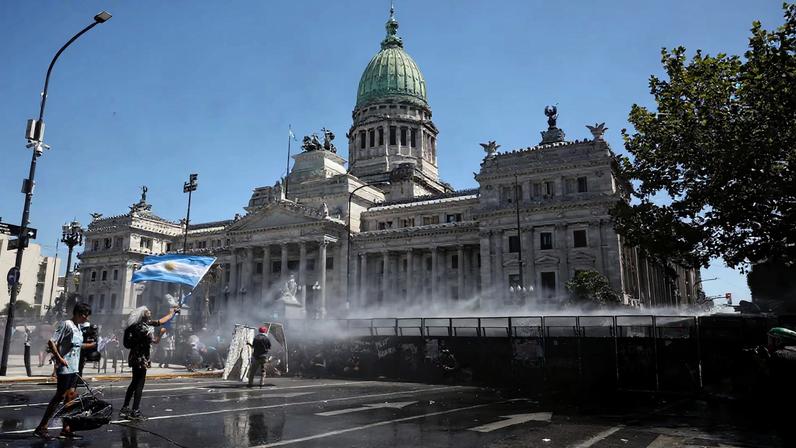 A demonstrator holds a flag as police use a water cannon during a protest outside Argentina's National Congress on the day senators vote on a labor reform law proposed by President Javier Milei's libertarian government to attract investment and revive growth, and which unions say will roll back workers' rights, in Buenos Aires, Argentina February 27, 2026. REUTERS/Agustin Marcarian